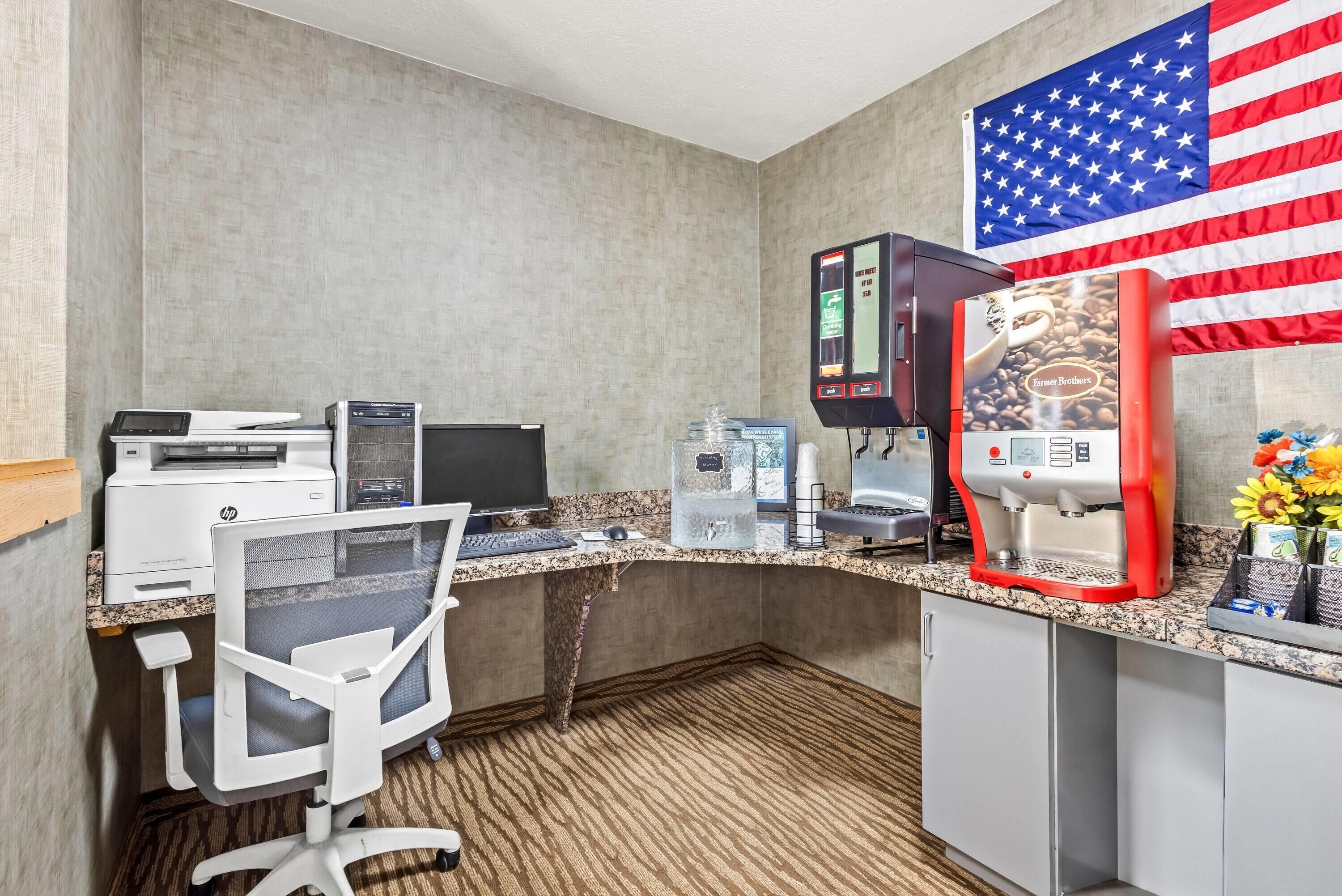 A hotel room with a desk, HP printer, coffee machine, and an American flag.