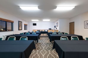 Conference room with rows of tables and chairs, carpeted floor, and a flat-screen TV.