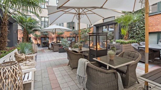 An outdoor patio area with wicker furniture, a fire feature, and a large umbrella providing shade. - Best Western Plus Hotel Hebron (Copenhagen)