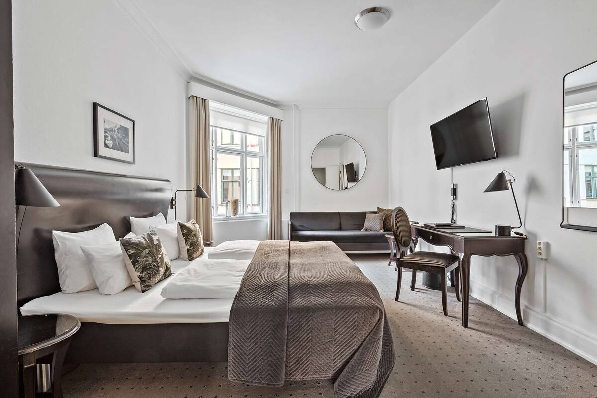 A hotel room with a bed, a desk, a chair, a TV, and a window.