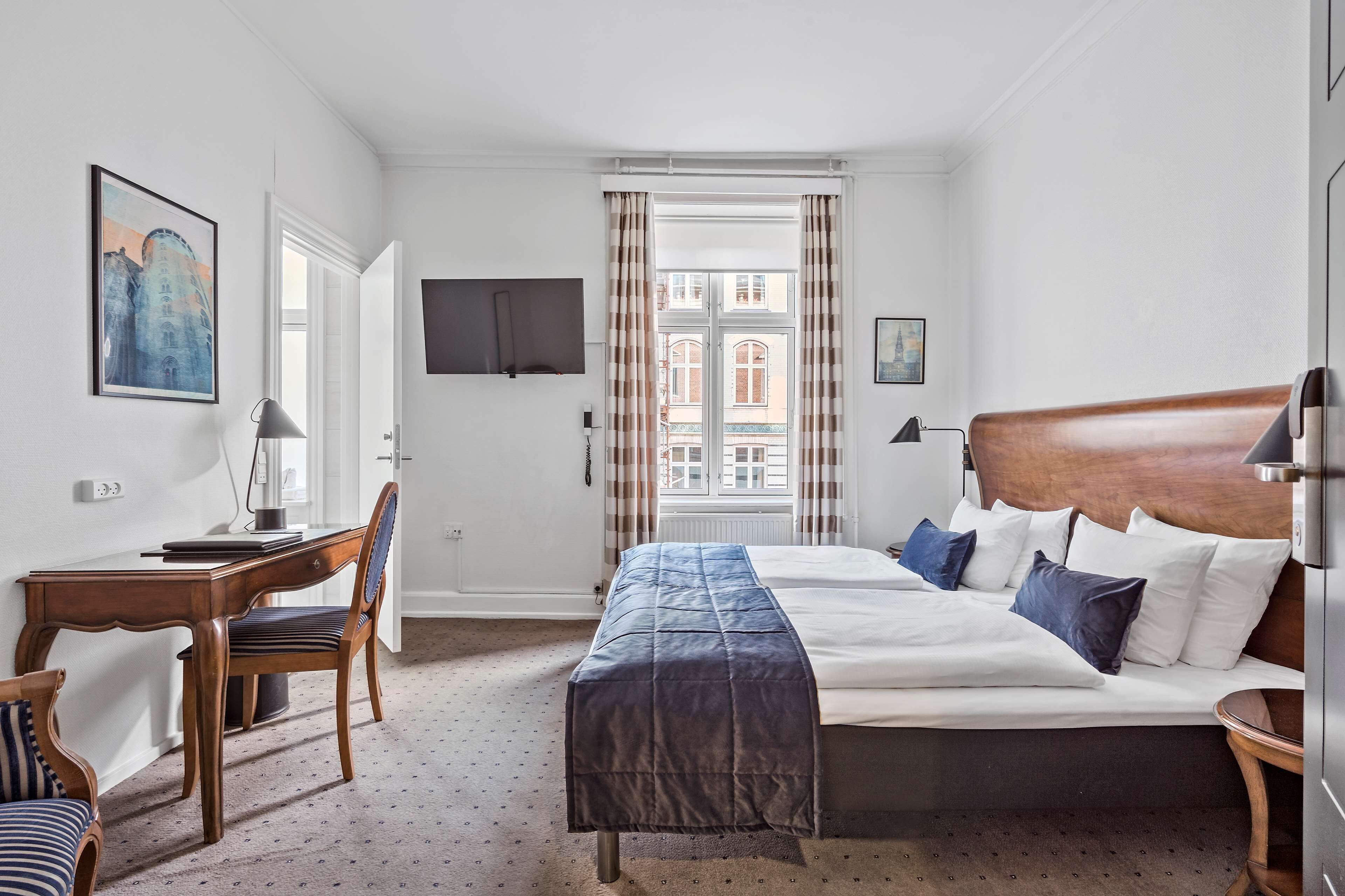 Een hotelkamer met een bed, een bureau, een stoel, een televisie en een raam met gordijnen.