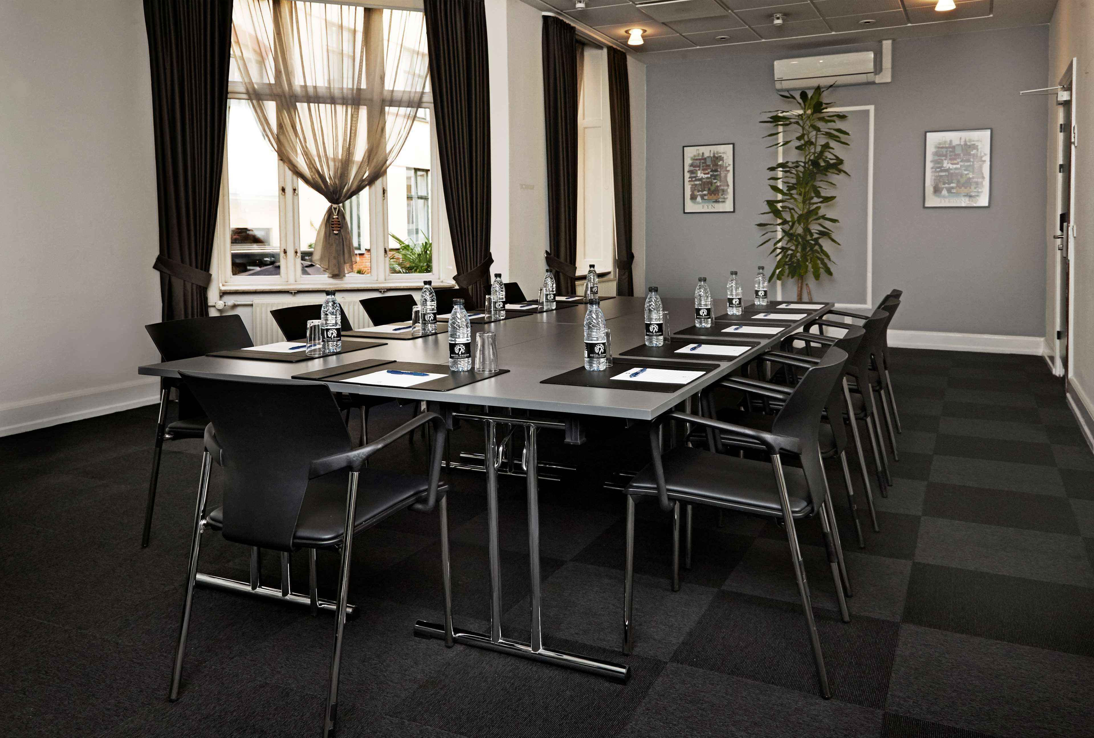 Een vergaderzaal met een lange tafel, stoelen, waterflesjes en een potplant.