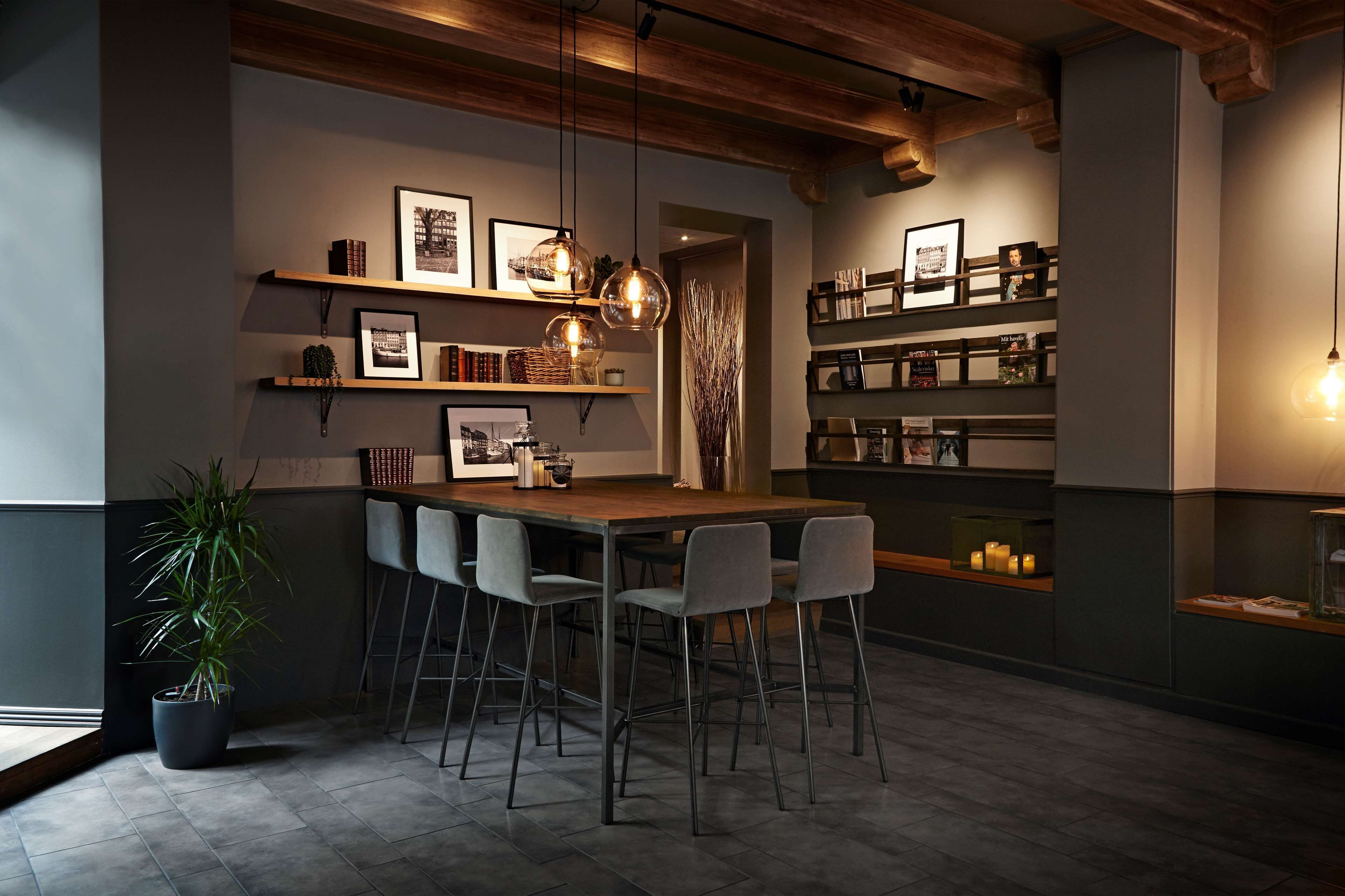 A modern kitchen with a wooden island, bar stools, pendant lighting, and shelves with framed pictures and books.