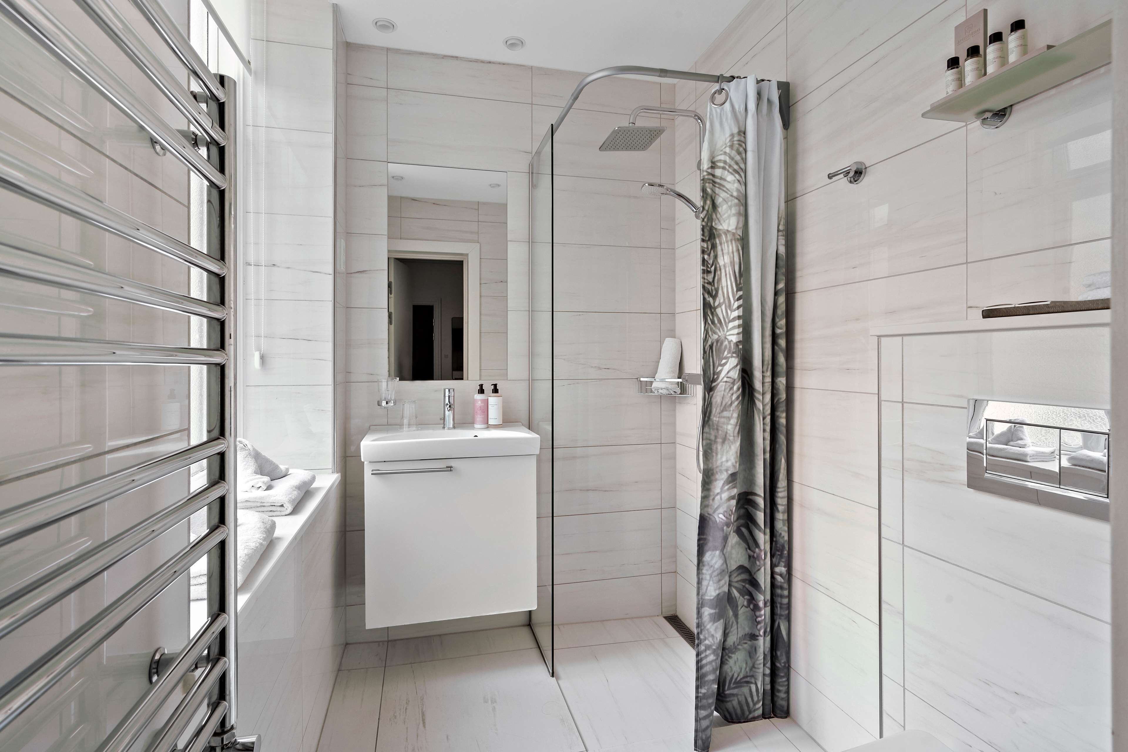 A modern bathroom with a glass shower enclosure, a white sink with toiletries, and a mirror above the sink.
