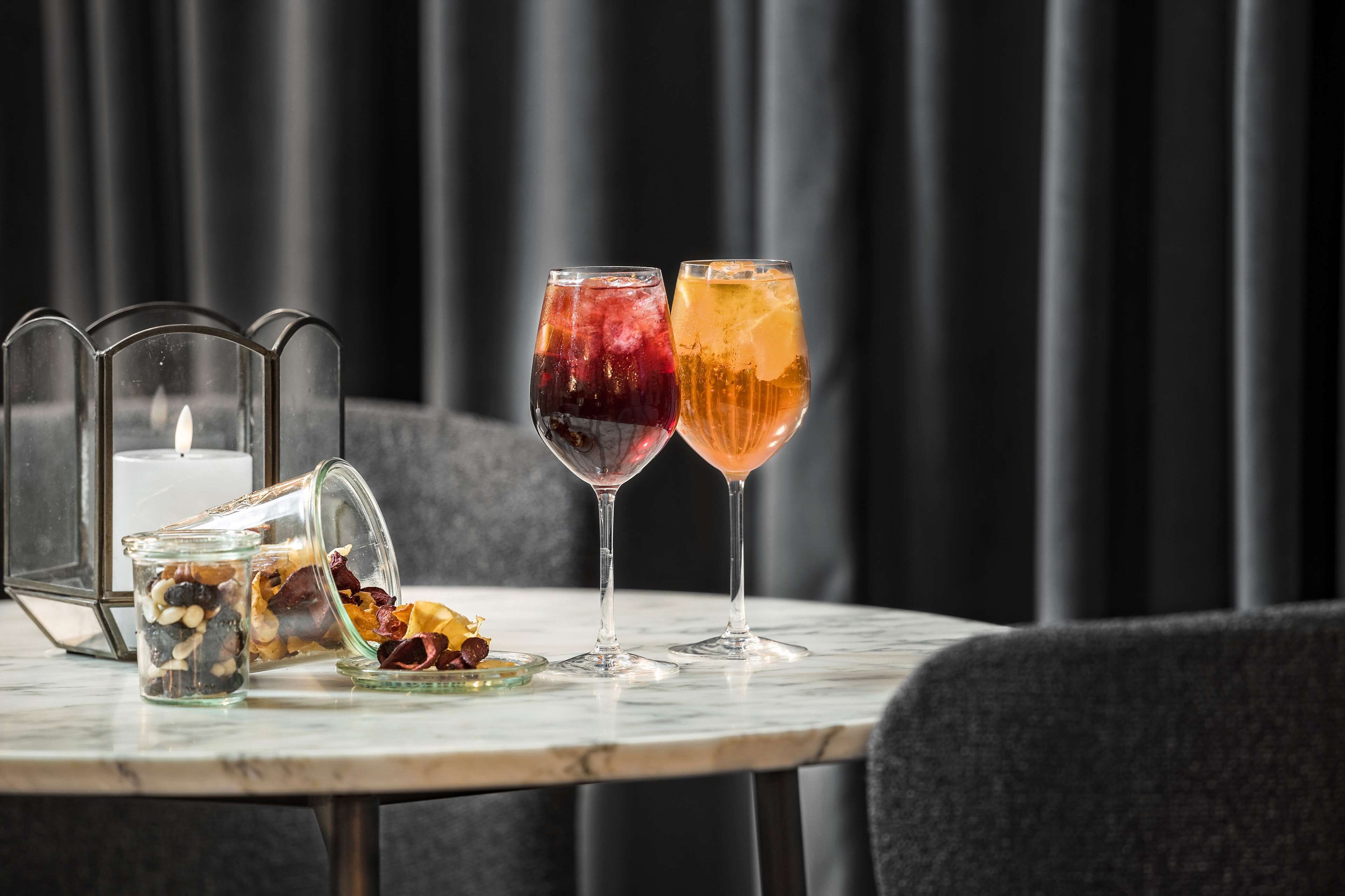 A table with two glasses of beverages, a candle, and a glass jar with dried fruits.