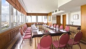 A conference room with a long table, multiple chairs, and large windows offering a city view.
