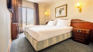 A hotel room with a large bed, a desk, a TV, and a window with curtains. - SANA Rex Hotel (Lisbon)