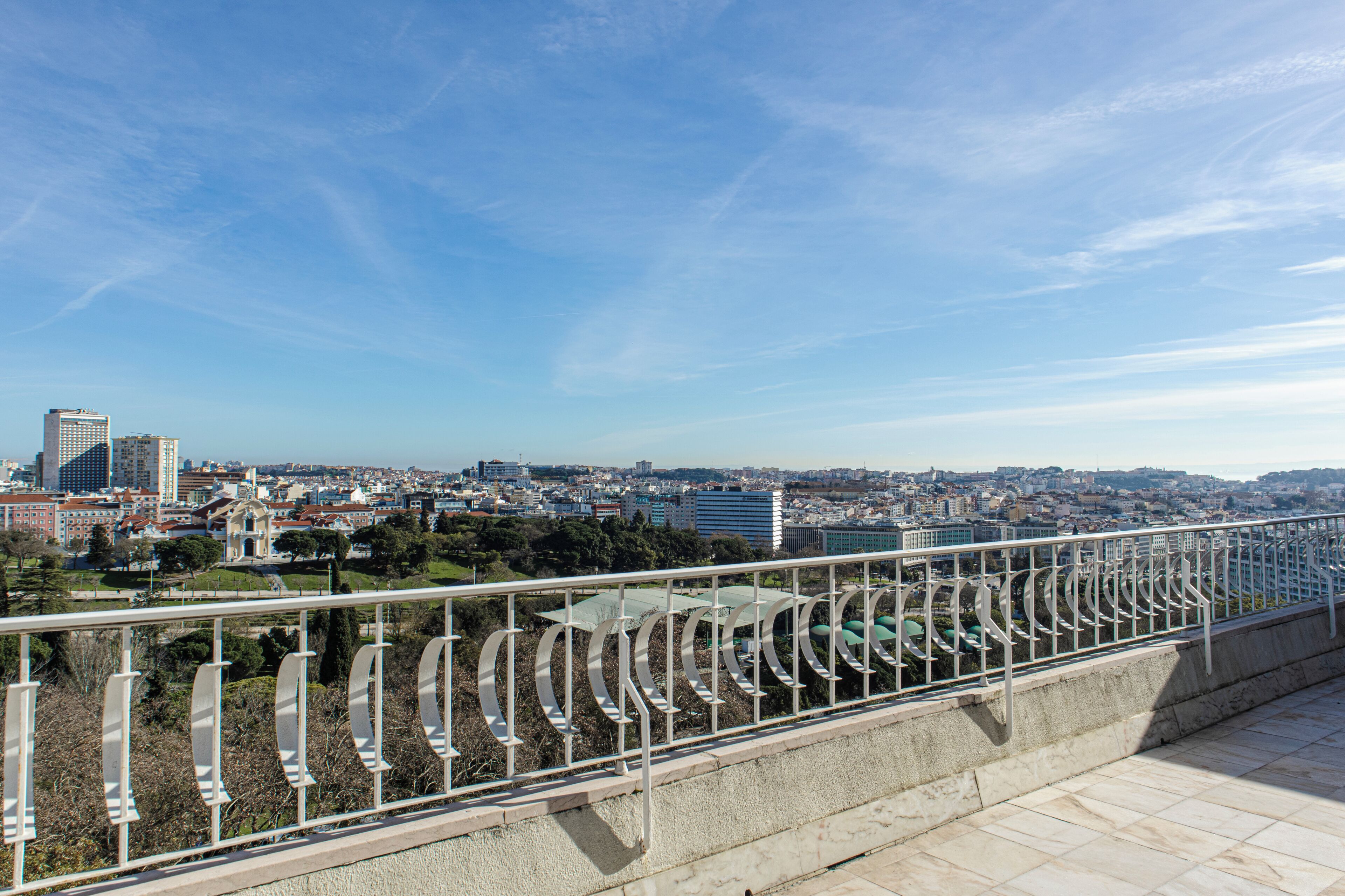 Une vue urbaine avec un ciel dégagé, une rambarde en métal et des bâtiments à l’horizon.