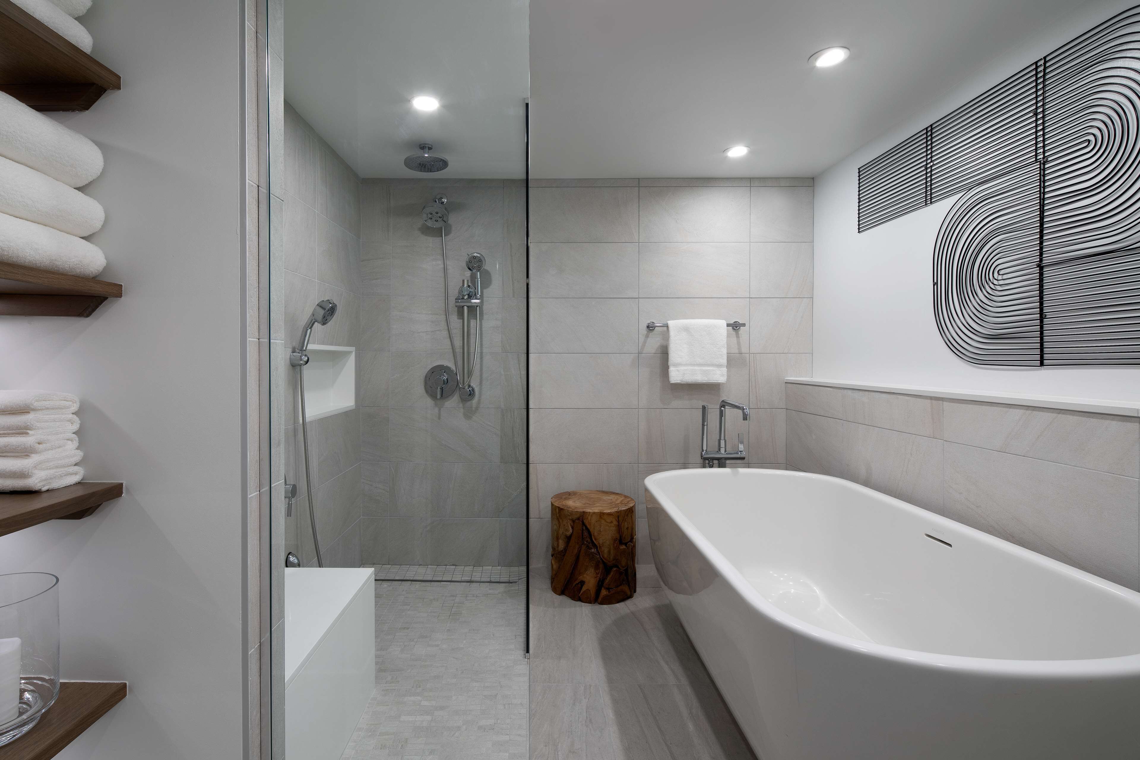 Un baño moderno con ducha acristalada, bañera independiente y taburete de madera.