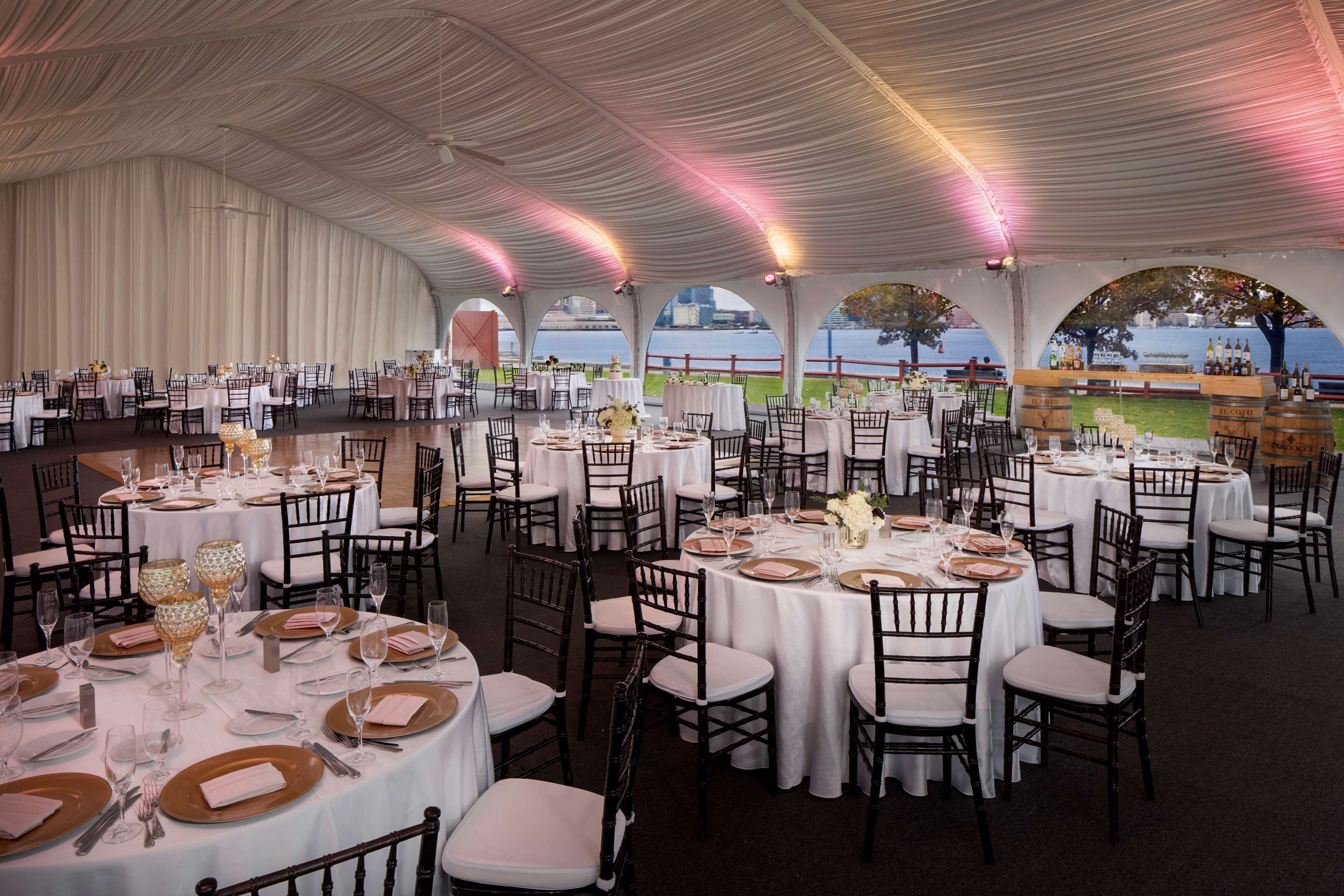 A tented dining area with round tables set for a formal event, featuring white tablecloths and gold accents.