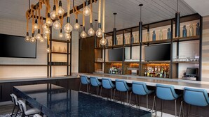 Een moderne bar met een lange toonbank, blauwe stoelen en diverse flessen en glazen.