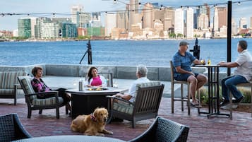 A waterfront patio with outdoor seating and a city skyline in the background.