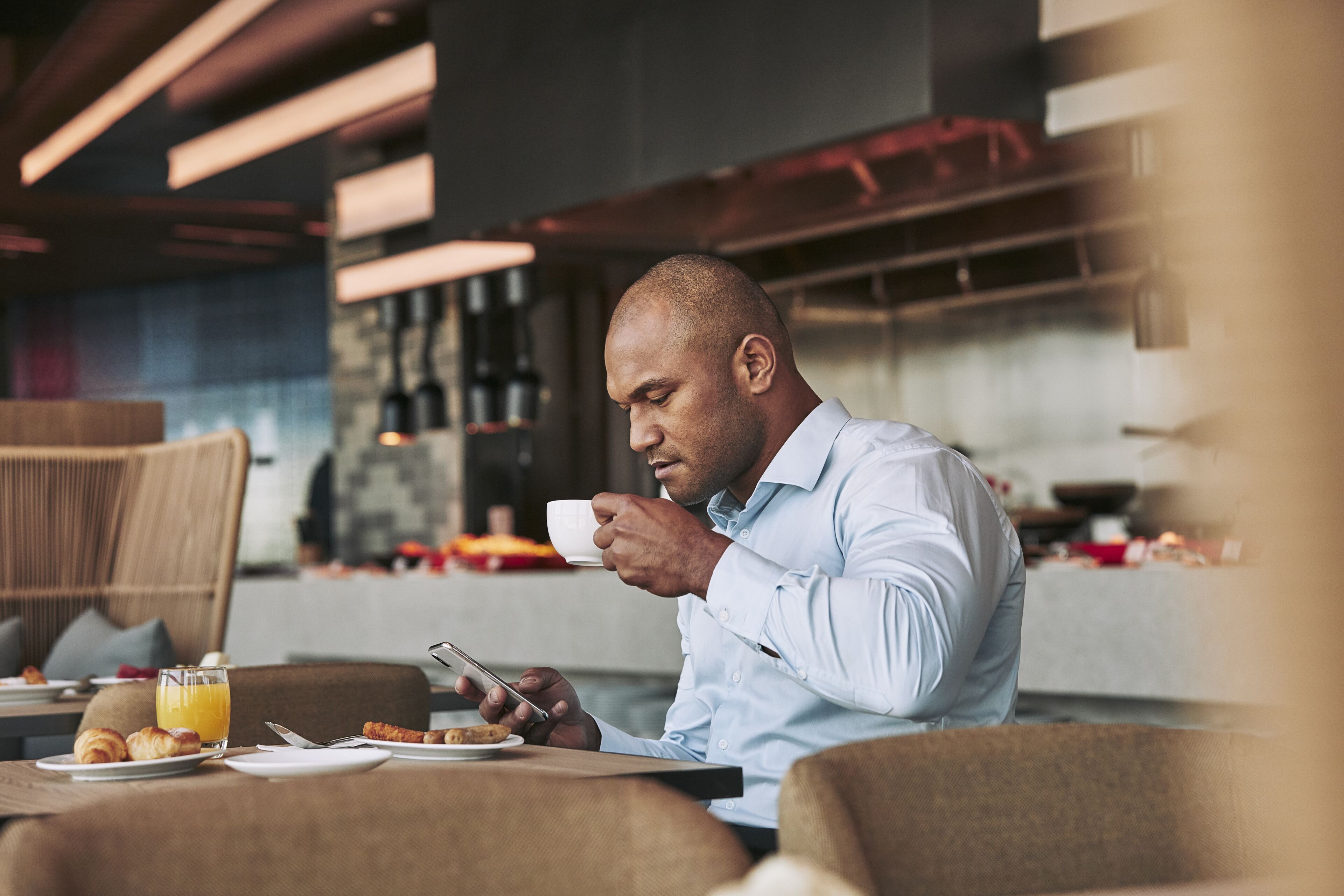Um homem sentado à mesa com comidas de café da manhã e um copo de suco de laranja.