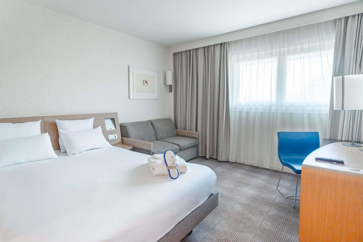 Quarto de hotel com uma cama, um sofá, uma escrivaninha e uma cadeira.