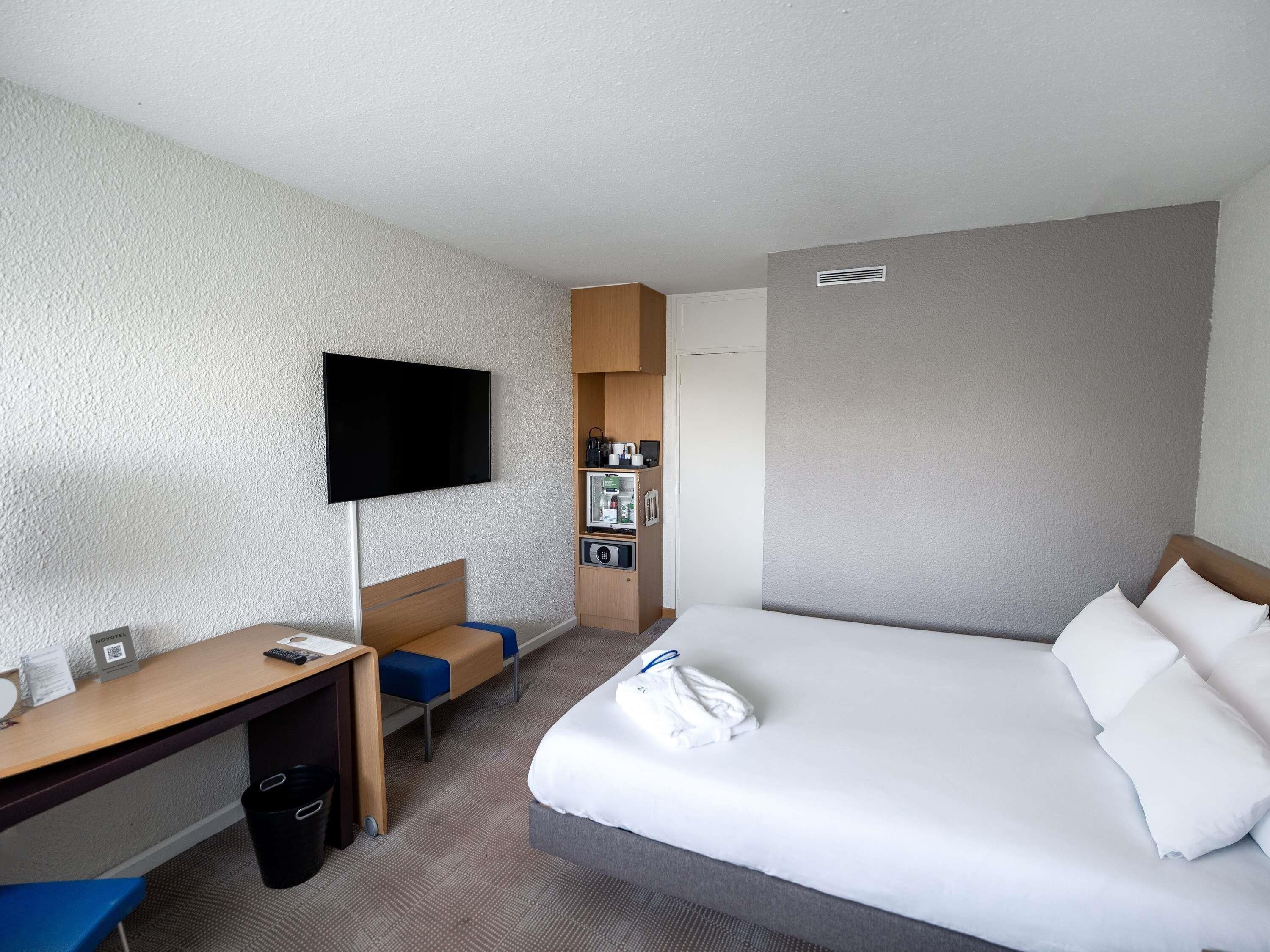 A hotel room with a bed, a desk, a TV, a minibar, and a shower area.