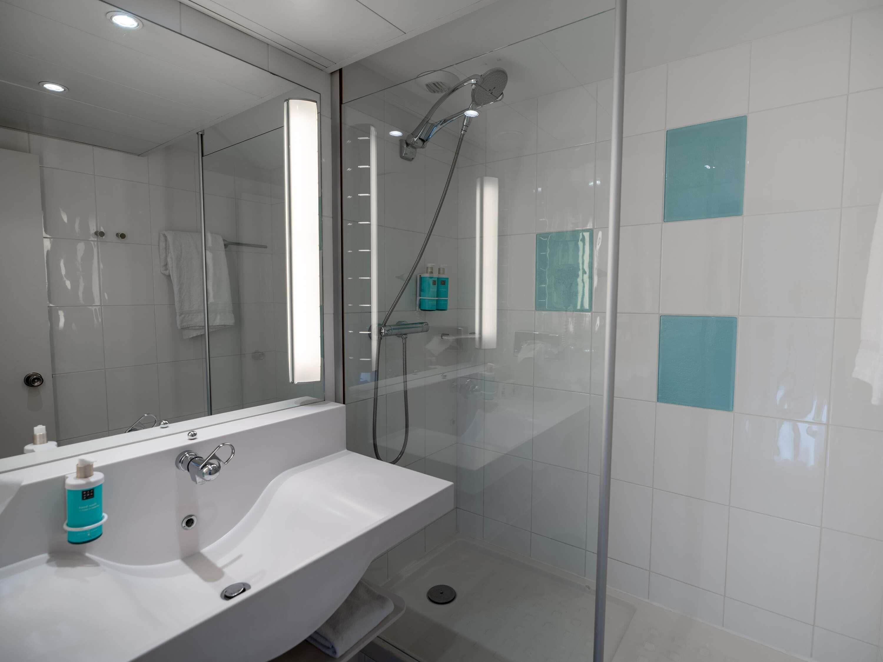 Une salle de bain moderne avec une douche à parois de verre, un lavabo blanc et un miroir.