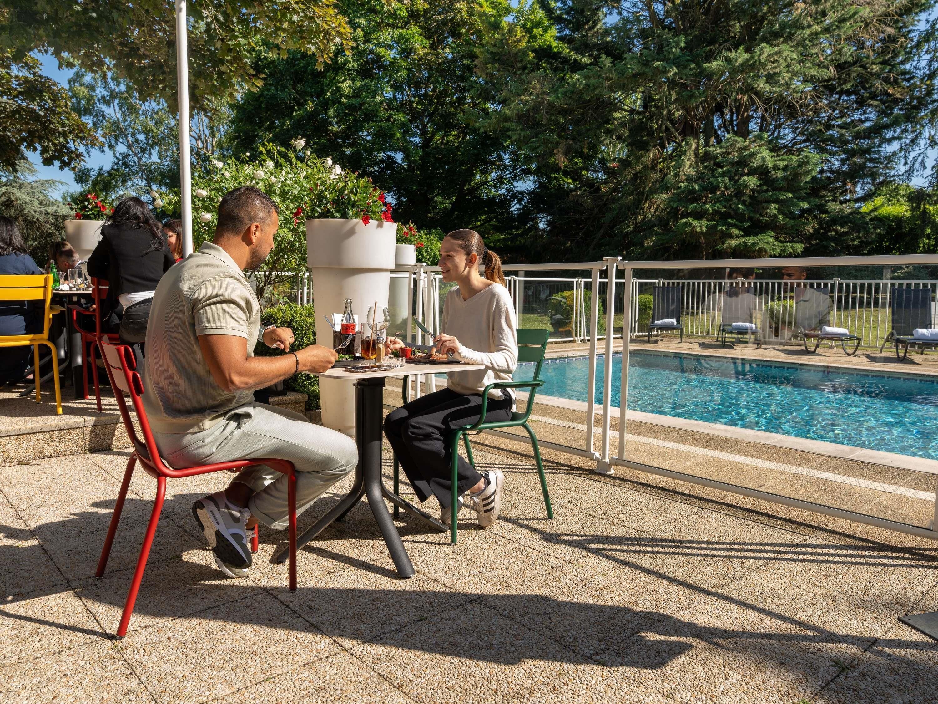 An outdoor dining area with a pool in the background.