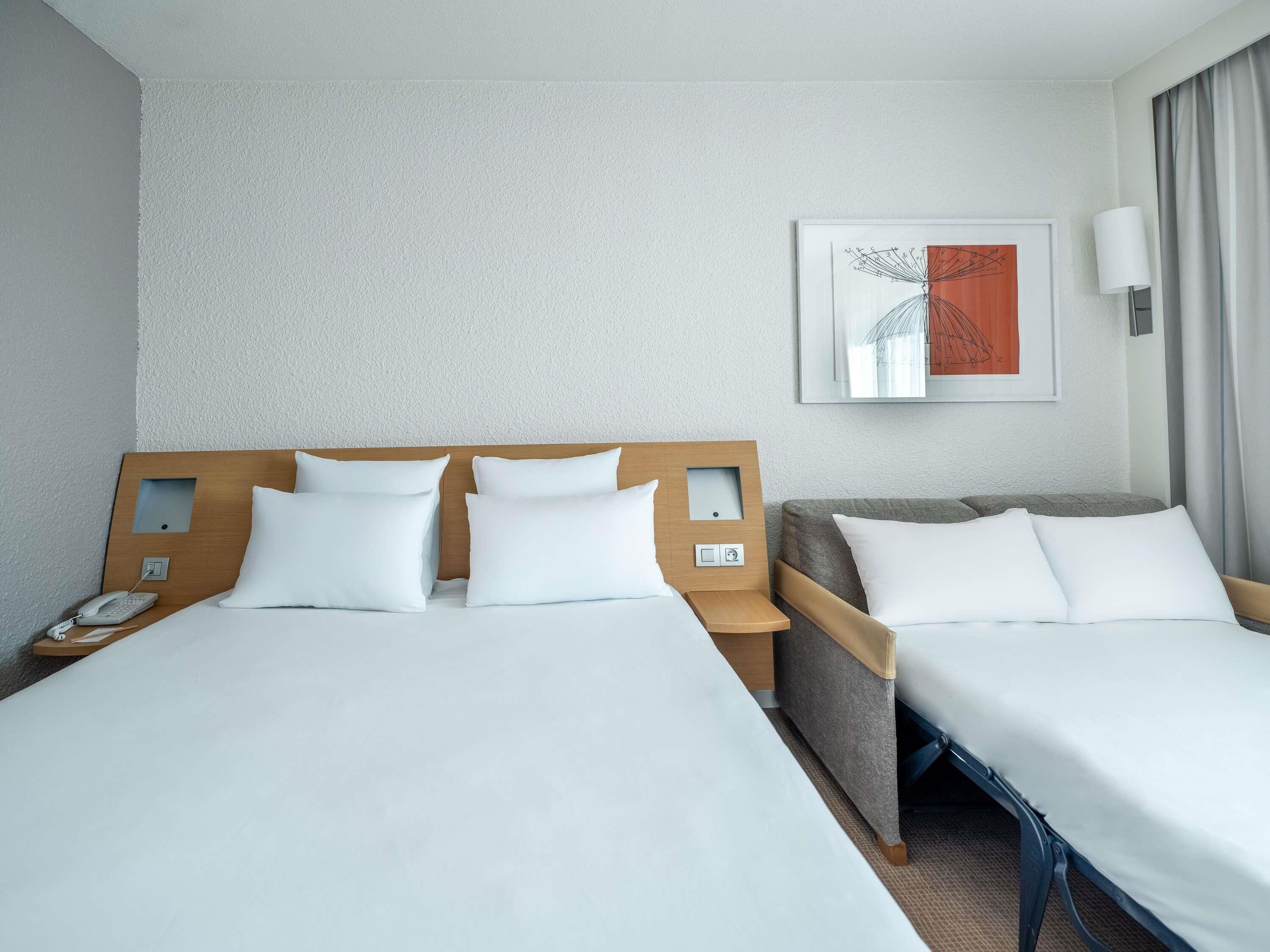 Een hotelkamer met twee bedden, een nachtkastje met een telefoon, een lamp en een lijst met kunst aan de muur.
