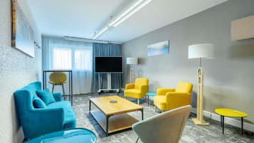 A modern hotel room with a sofa, chairs, a coffee table, a TV, and a lamp.