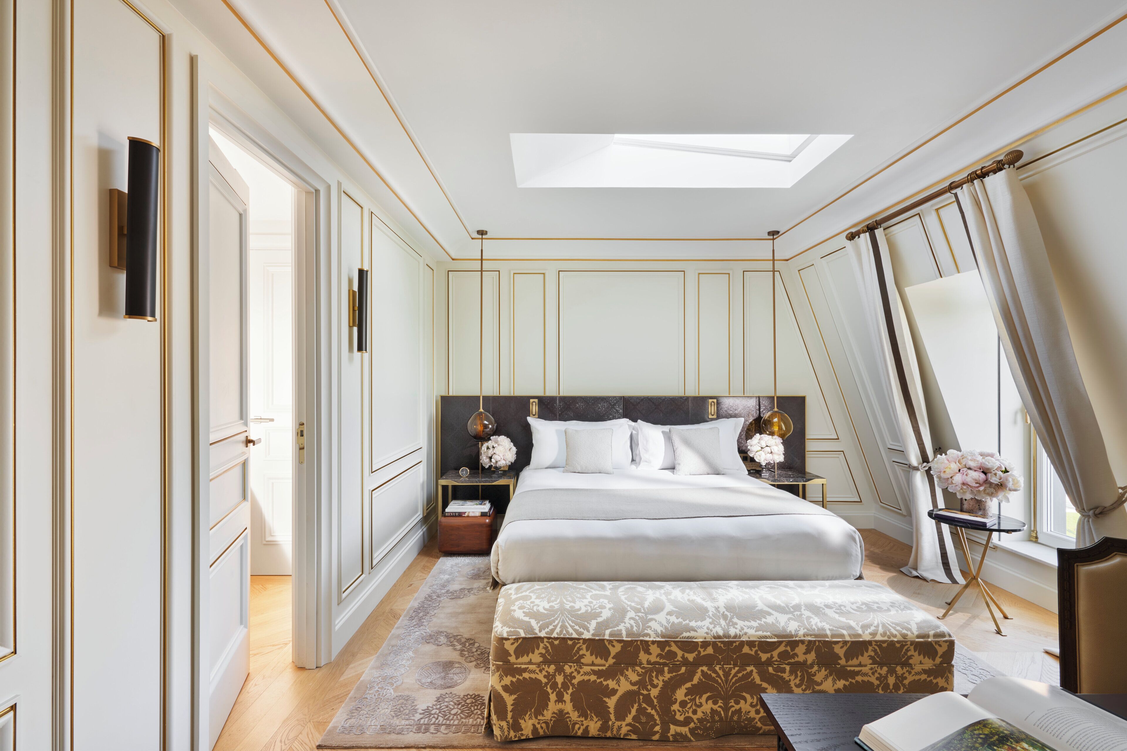 A bedroom with a large bed, bedside tables, a nightstand, a window with curtains, and a skylight.
