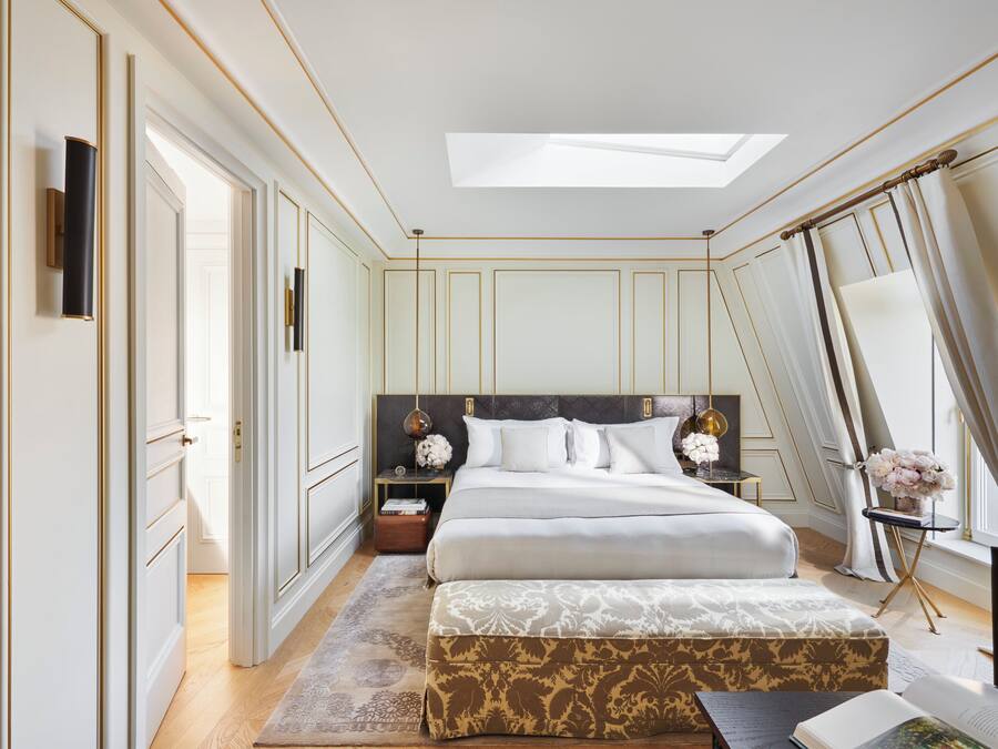 A bedroom with a large bed, bedside tables, a nightstand, a window with curtains, and a skylight.