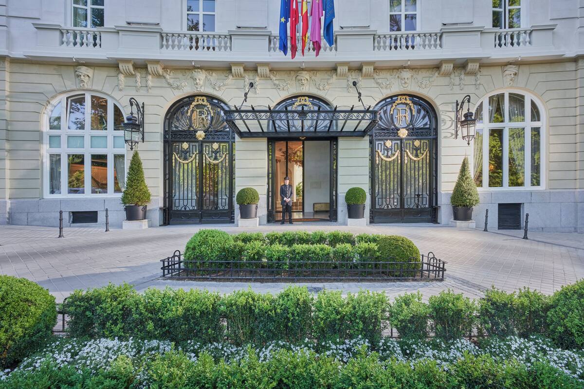 A grand building with ornate black gates, a central entrance, and a well-maintained garden.