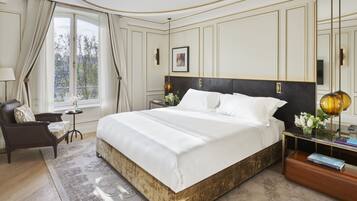 Un dormitorio lujoso con una cama grande, una mesita de noche, una silla y vistas al exterior a través de un ventanal.
