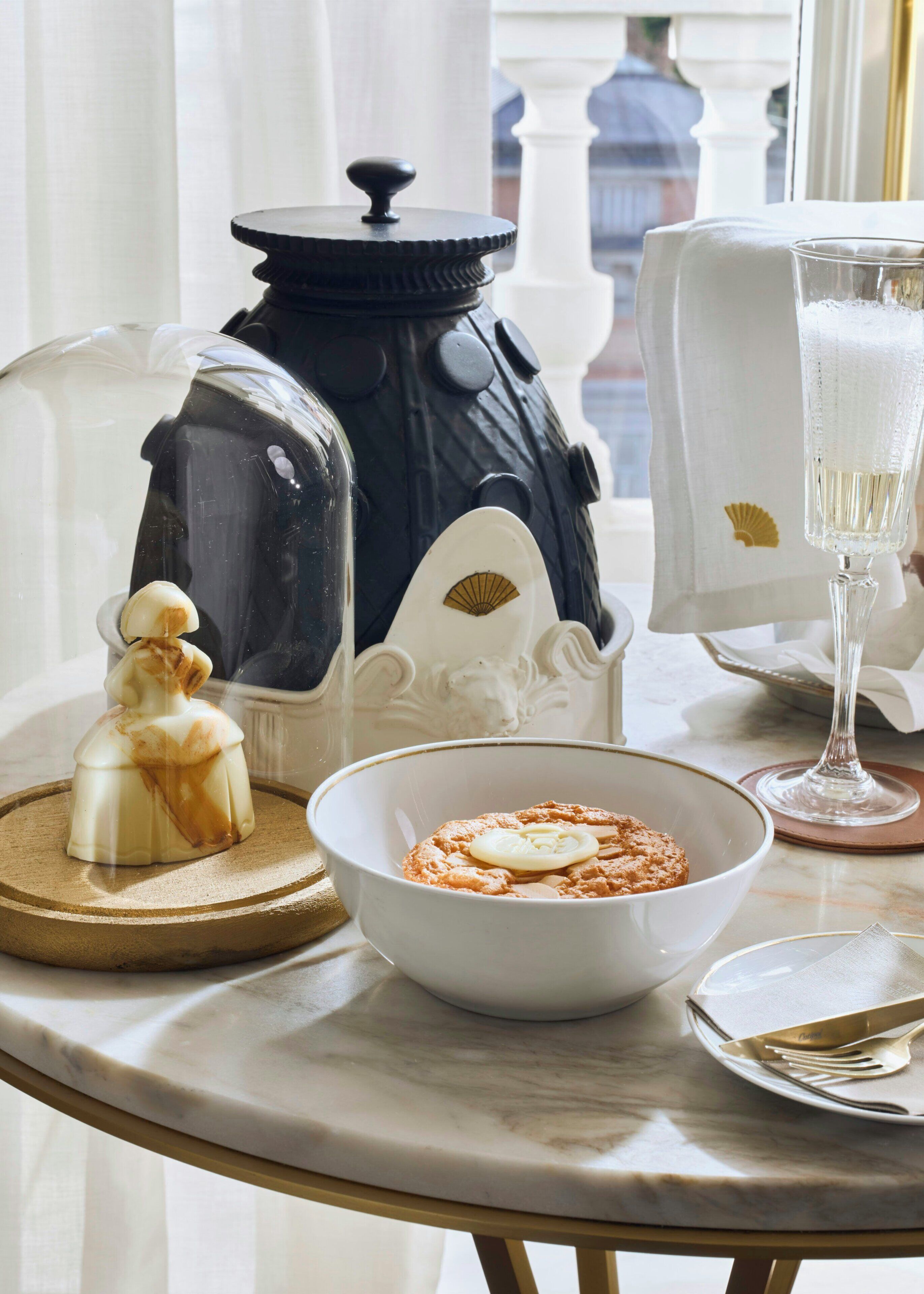 Uma mesa com uma tigela de comida, um copo de bebida, um frasco decorativo e uma pequena estatueta.