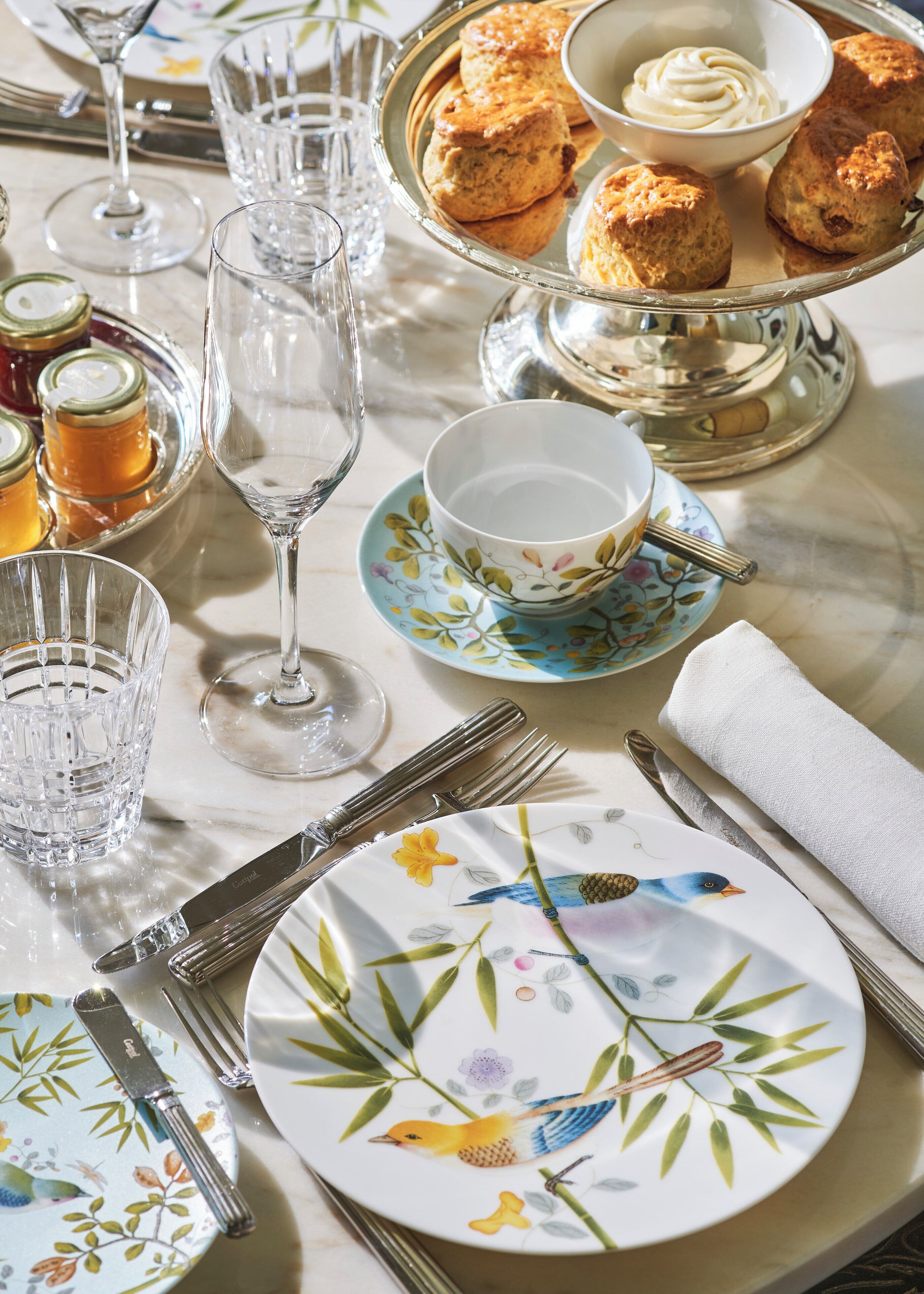 A table set with fine china, silverware, and scones, suggesting a formal dining experience.