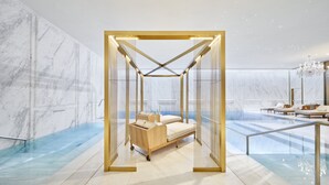Una lujosa habitación de hotel con una cama rodeada de vidrio, paredes de mármol y una zona de piscina.