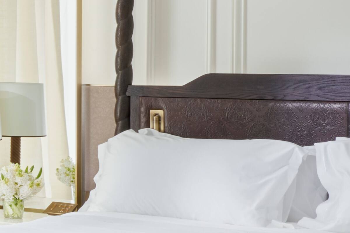 A hotel room with a bed, two bedside lamps, a nightstand with a clock, and a vase with flowers.