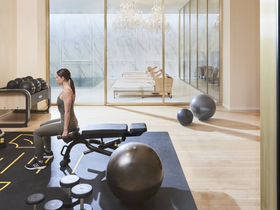 Una palestra moderna con attrezzi per esercizi, uno specchio grande e vista su una stanza bianca con un lampadario.