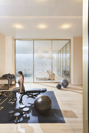 A modern gym with exercise equipment, a large mirror, and a view of a white room with a chandelier.