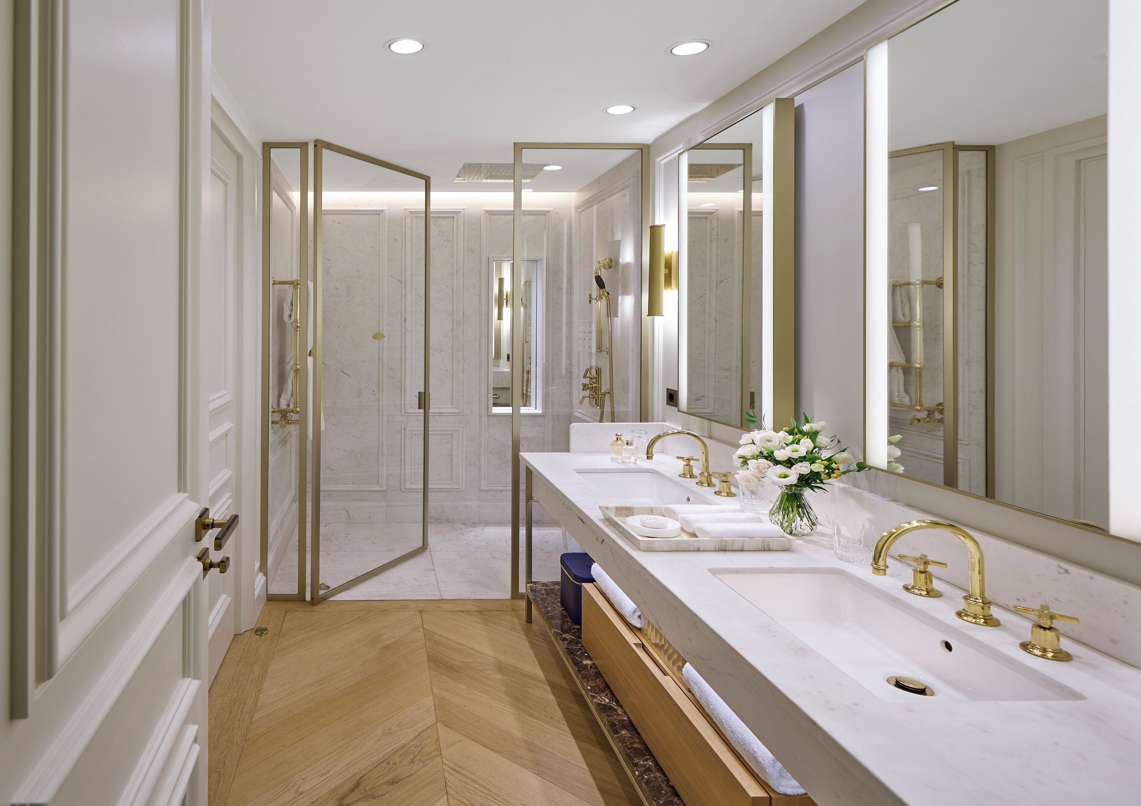 Ein luxuriöses Badezimmer mit drei Waschbecken, großen Spiegeln und einer Duschkabine.