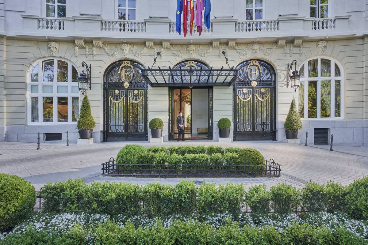 A grand building with ornate black gates, a central entrance, and a well-maintained garden.