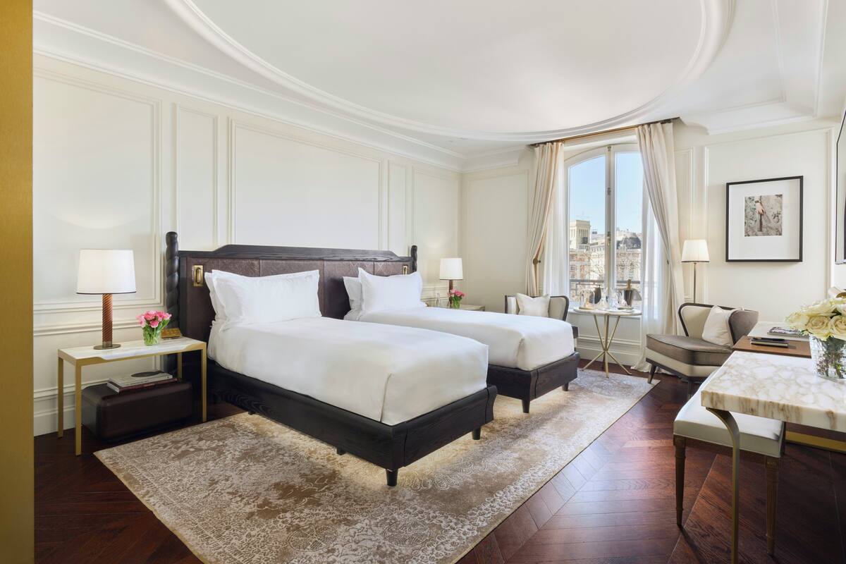 A hotel room with two beds, a sitting area, a dining table, and a view of the city.