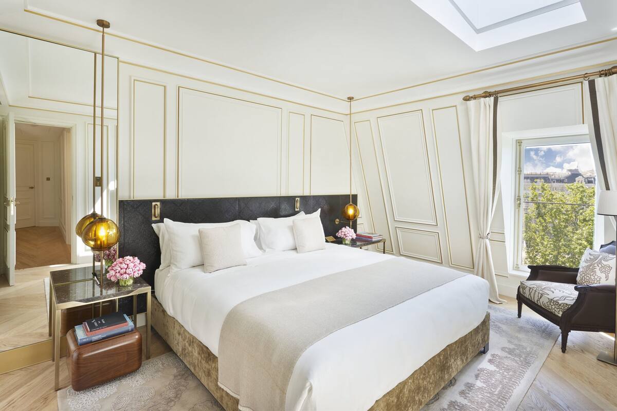 A spacious bedroom with a large bed, a nightstand, a reading lamp, and a view of the outdoors.