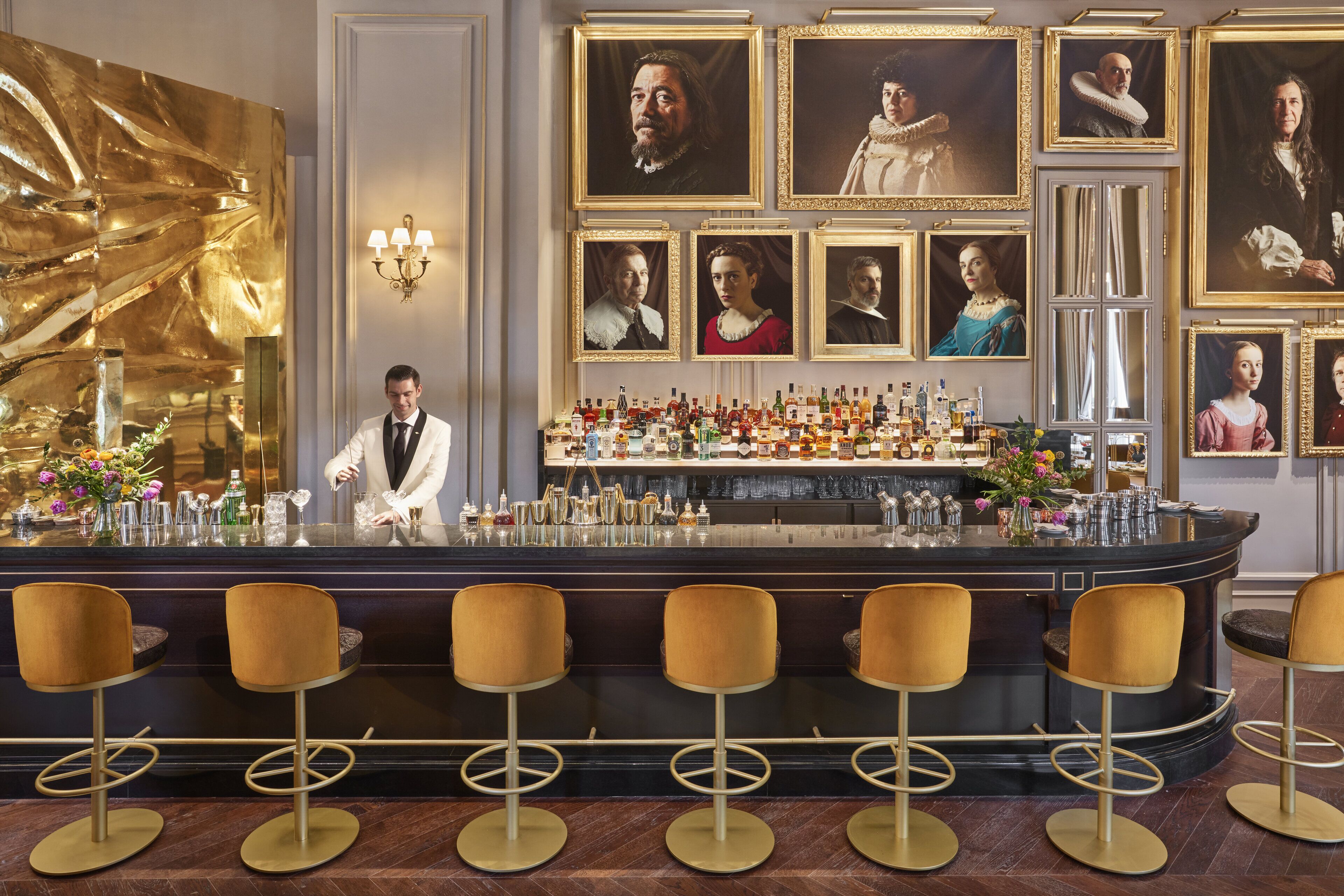 Uma área de bar com um bartender, banquetas e diversos tipos de garrafas e copos.