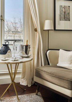 A room with a view of buildings, a table with a bottle of champagne, a lamp, and a sofa.