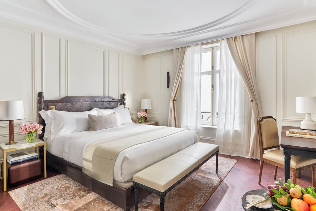 A well-appointed bedroom with a large bed, bedside tables, a bench, and a view of the outdoors.
