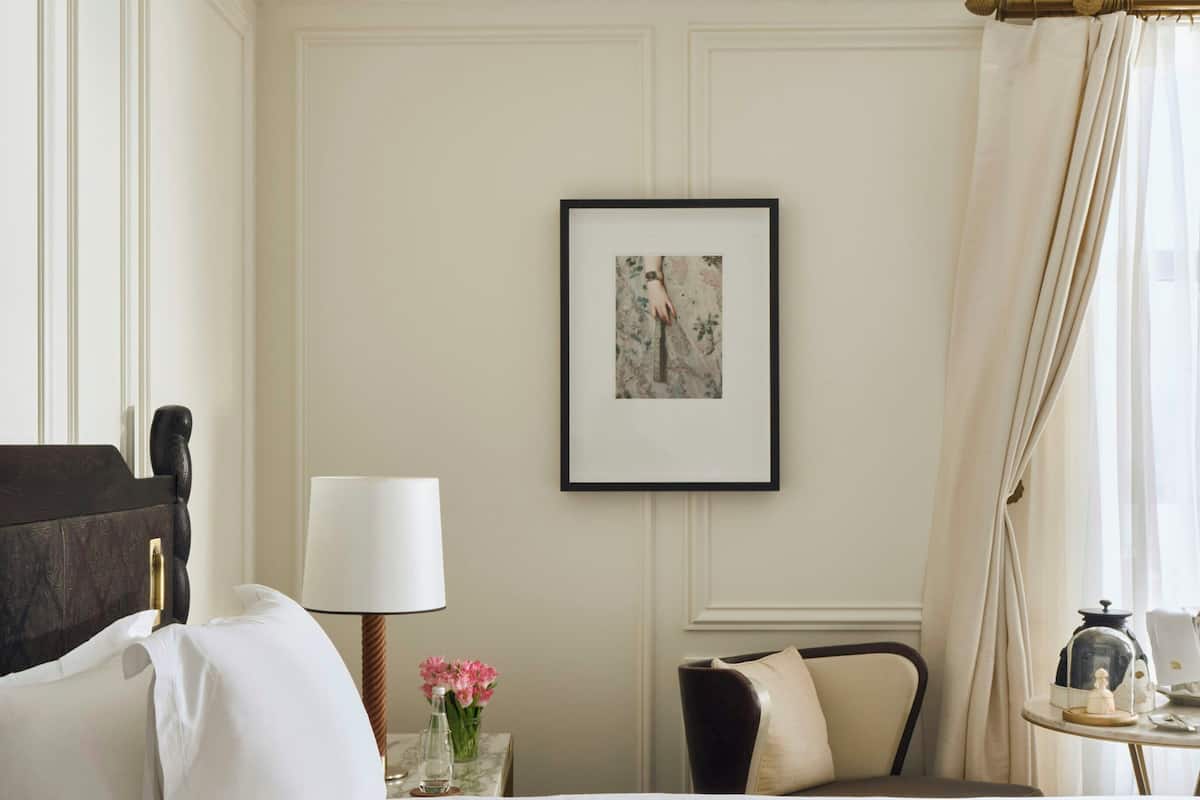 A hotel room with a bed, a chair, a table with a lamp, a picture on the wall, and a window with curtains.