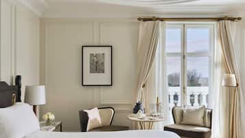 A hotel room with a bed, a chair, a small table with a lamp, a picture on the wall, and a window with curtains.