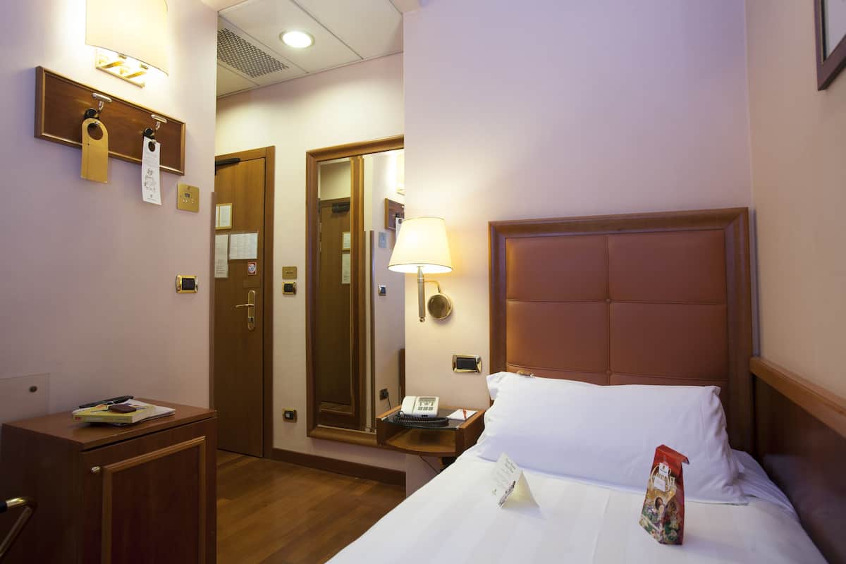 A hotel room with a bed, bedside table, lamp, and a mirror.