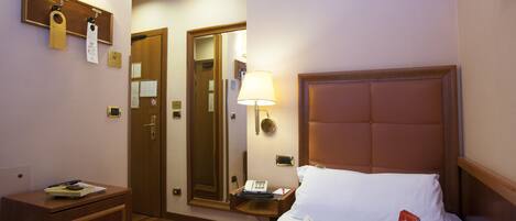 A hotel room with a bed, bedside table, lamp, and a mirror.