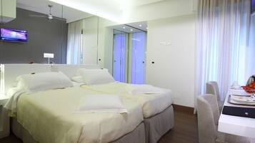 Una habitación de hotel moderna con una cama grande, un escritorio con una computadora portátil, un televisor y un espejo.