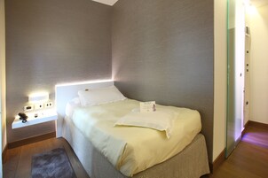 A neatly made bed with white linens, a bedside table with a lamp, and a small rug on the floor.