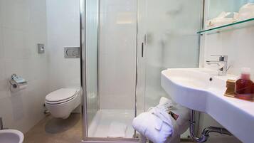 Een moderne badkamer met een douche met glazen wand, een wit toilet, een wastafel met spiegel en een handdoekrek.