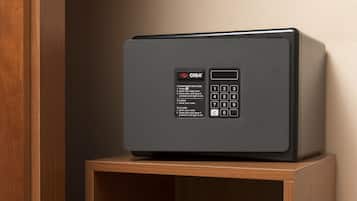 A black CISA safe on a wooden shelf in a room with a wooden door and a plain wall.