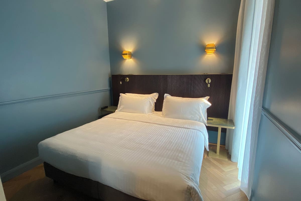 A neatly made bed in a room with blue walls, two bedside tables, and wall-mounted lights.