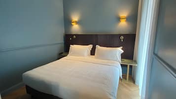 Een netjes opgemaakt bed in een kamer met blauwe wanden, twee nachtkastjes en wandlampen.